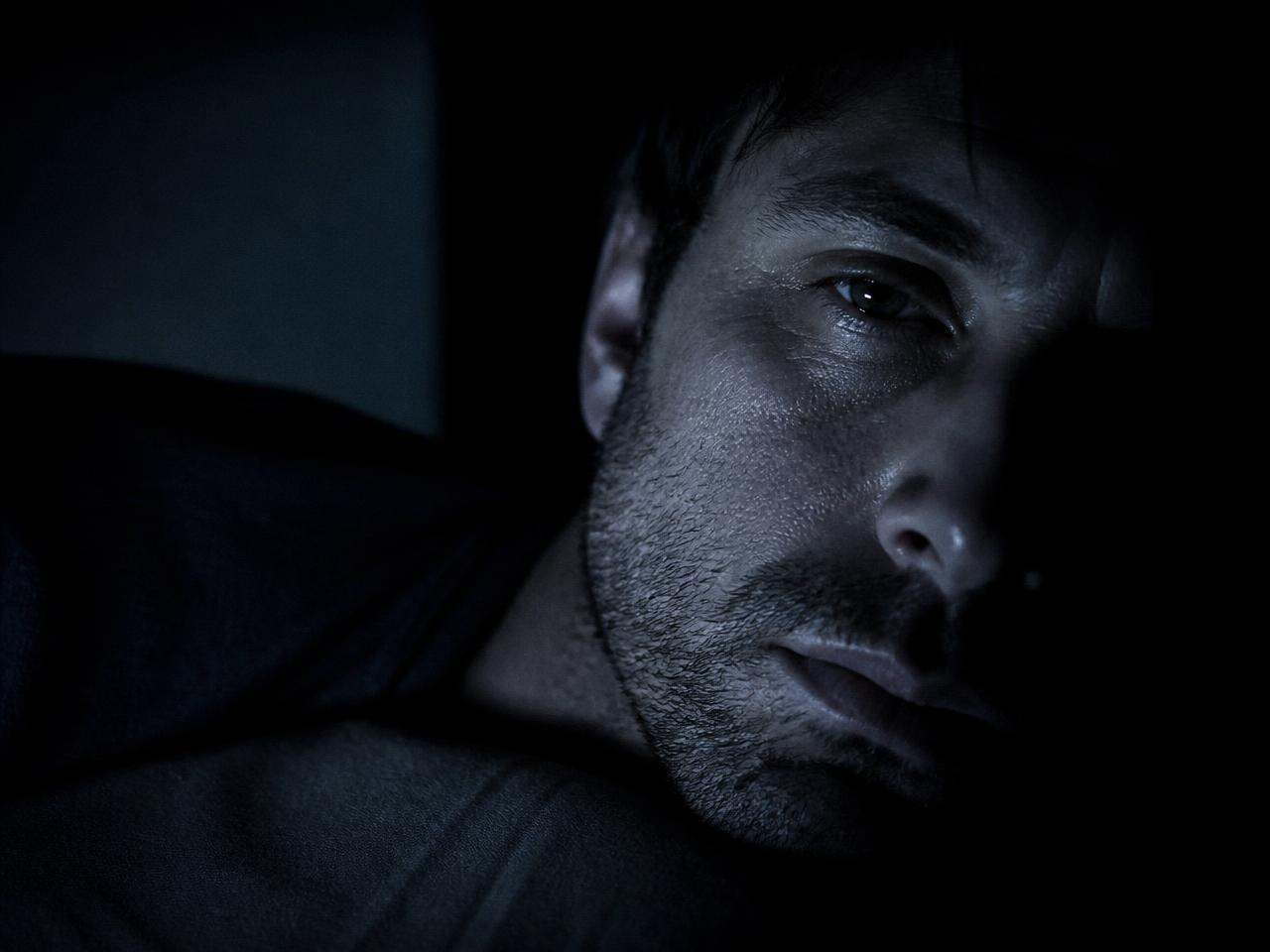 A man's face lit by phone glow in a dark room at 1am